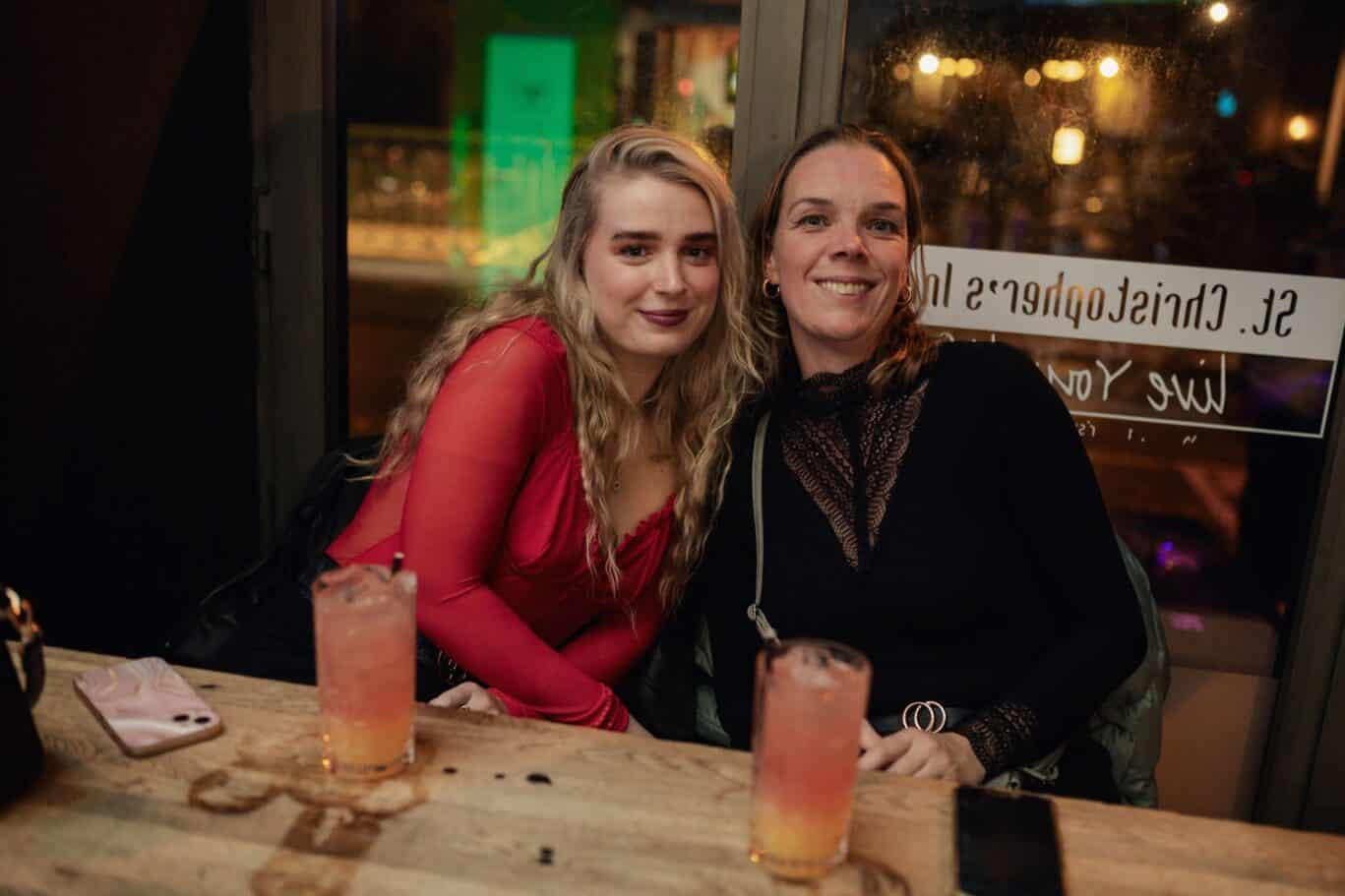 Two women smiling at a table in a lively bar or restaurant in Berlin.