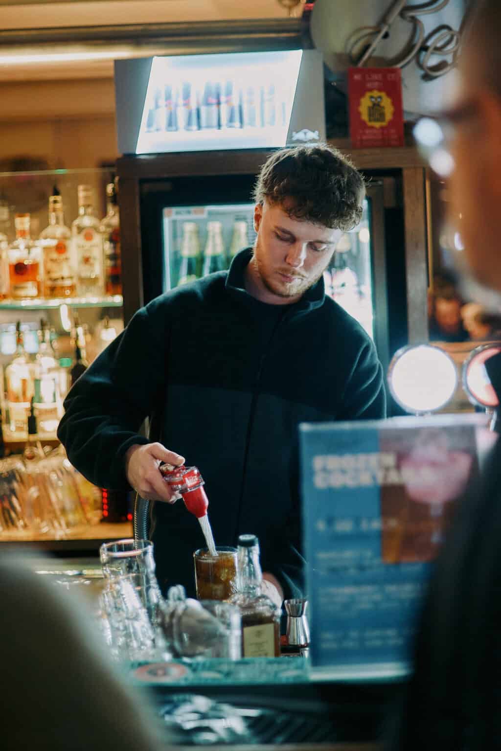 Young man pouring a drink at the bar in Alexanderplatz, Berlin.