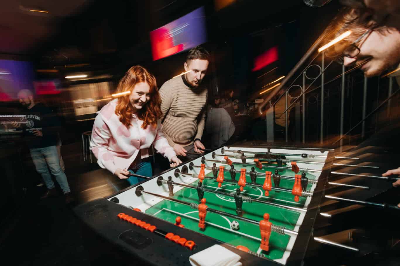 People playing foosball at Alexanderplatz hostel in Berlin, lively atmosphere.