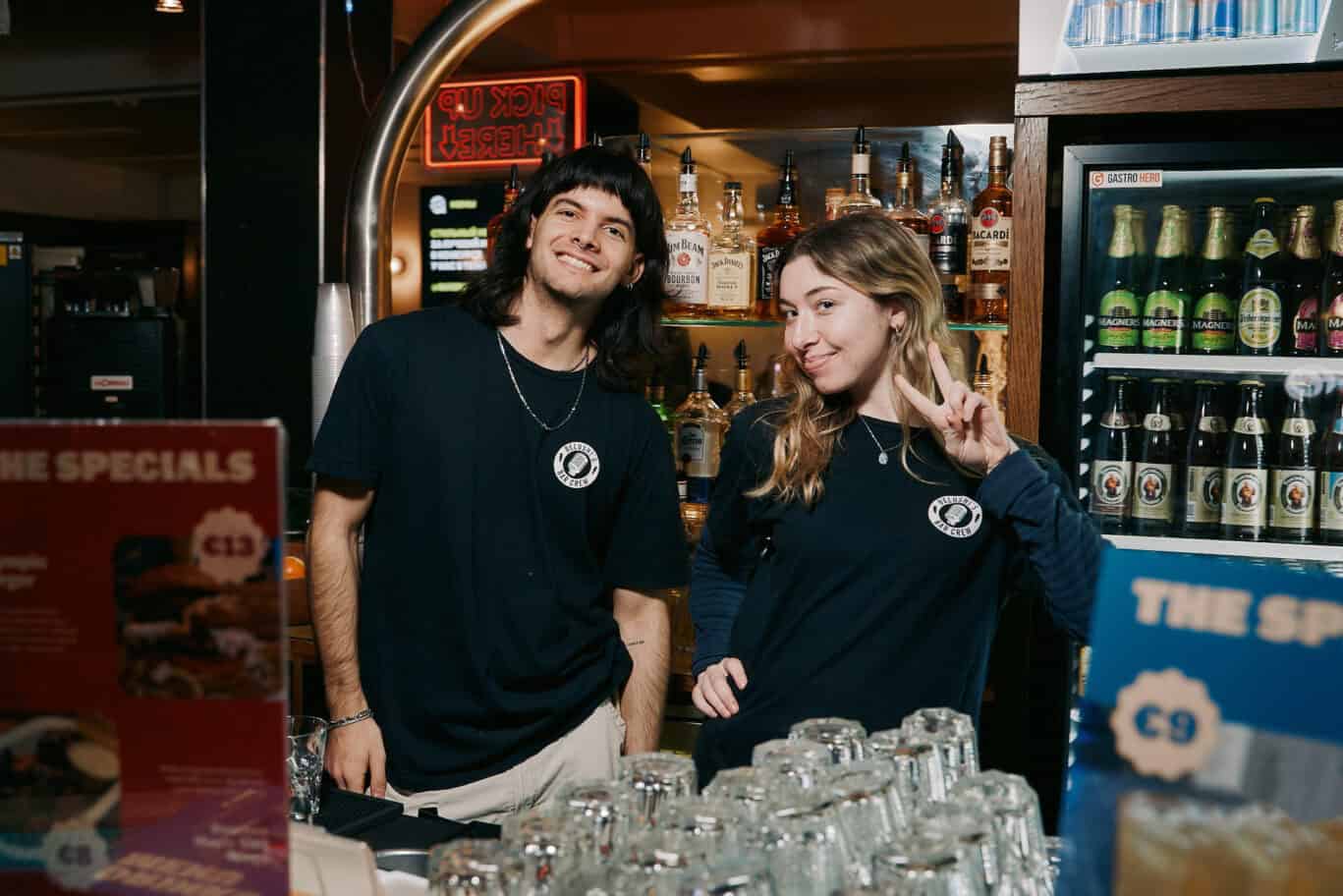 Friendly bar staff at Alexanderplatz Hostel, Berlin, smiling and making a peace sign.