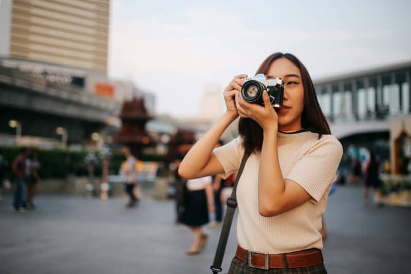 Young woman taking photos with a camera at Flying Pig Uptown hostel, urban setting in the background.