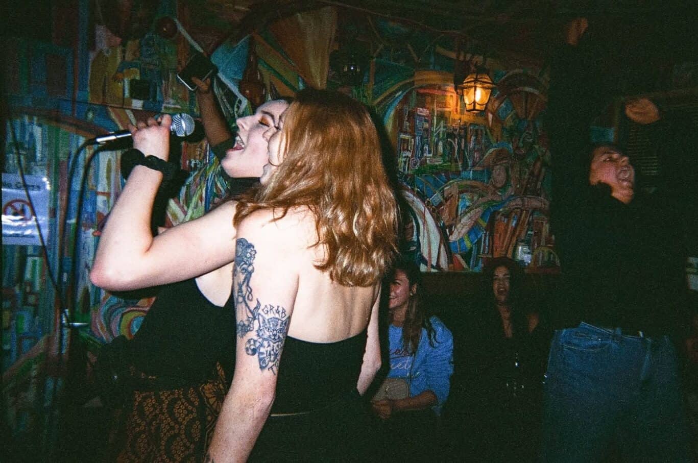 Lively woman singing with microphone at Flying Pig Uptown Hostel, vibrant bar scene.