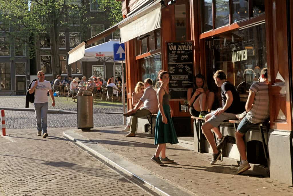People relaxing outside Flying Pig Uptown hostel in a lively city street.