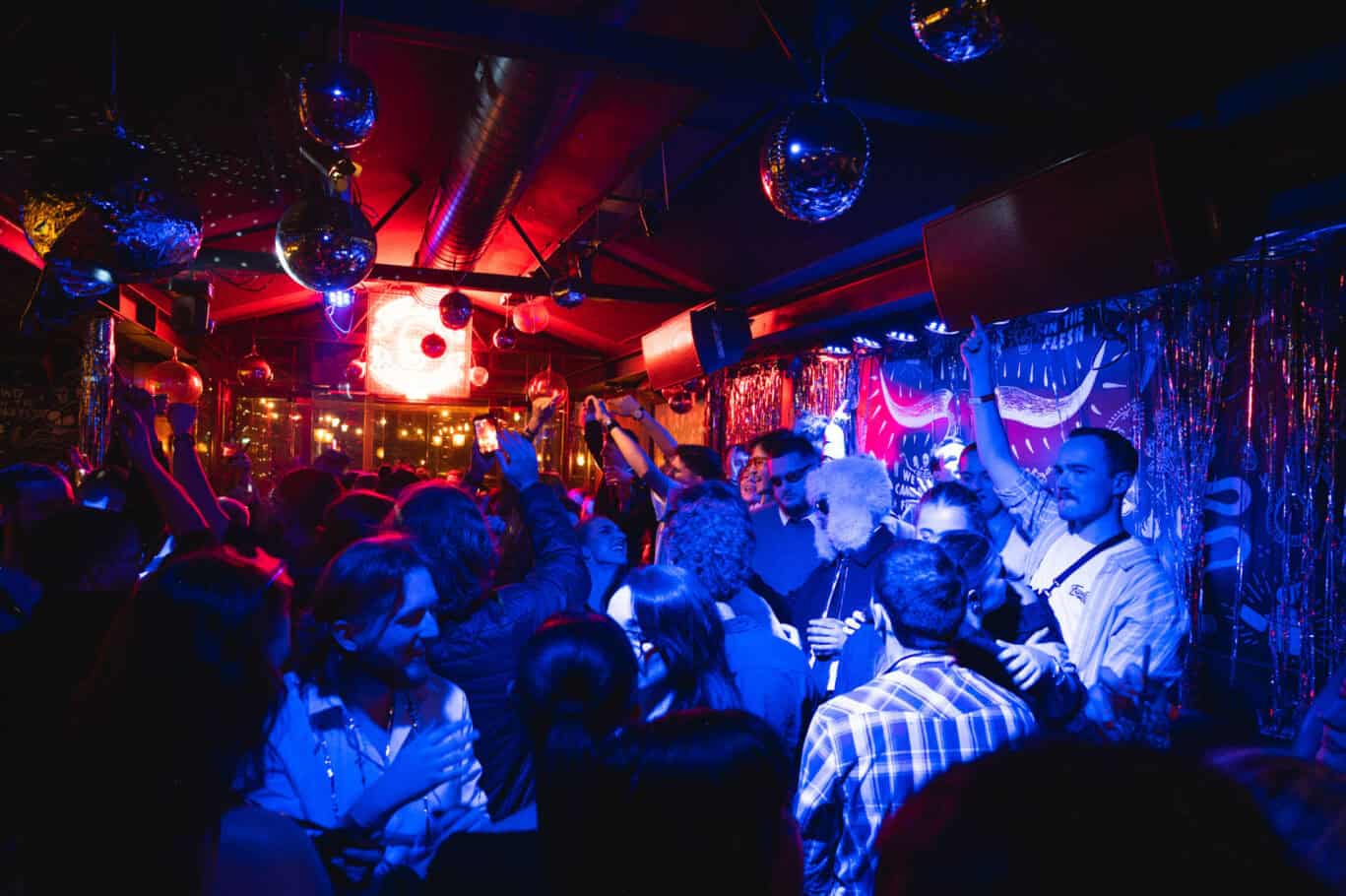 Vibrant nightlife scene at Winston Hostel in Amsterdam with lively crowd and colourful lighting.