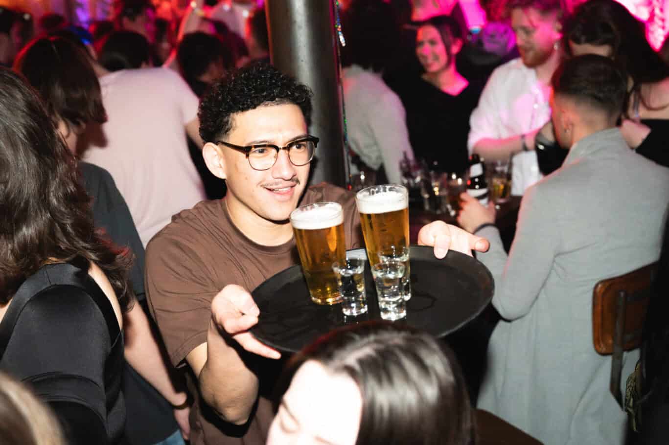 Young man serving drinks at Winston Hostel Amsterdam's lively bar area.