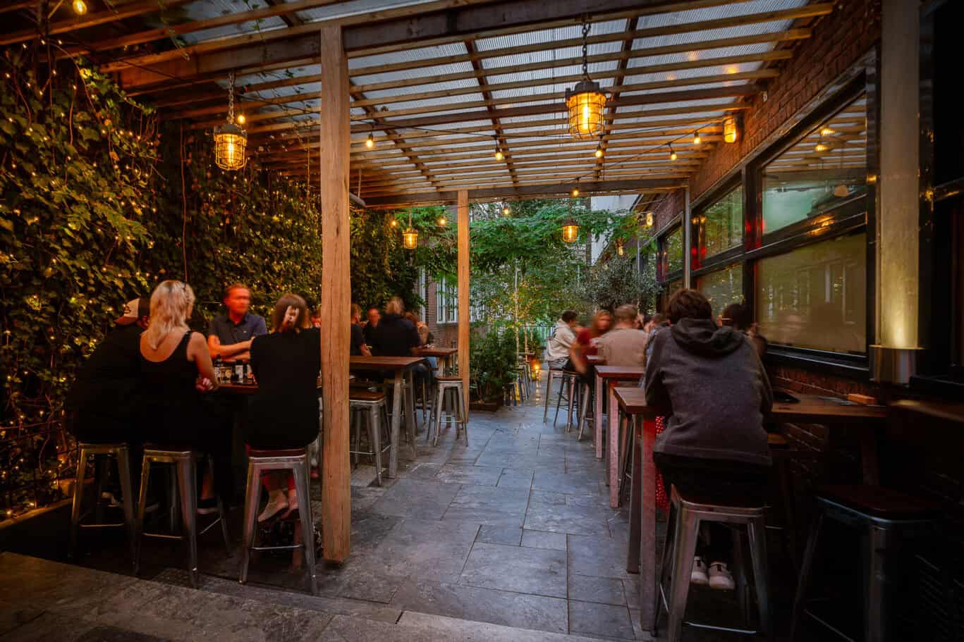 Outdoor dining area at Winston Hostel in Amsterdam with guests enjoying evening meals.