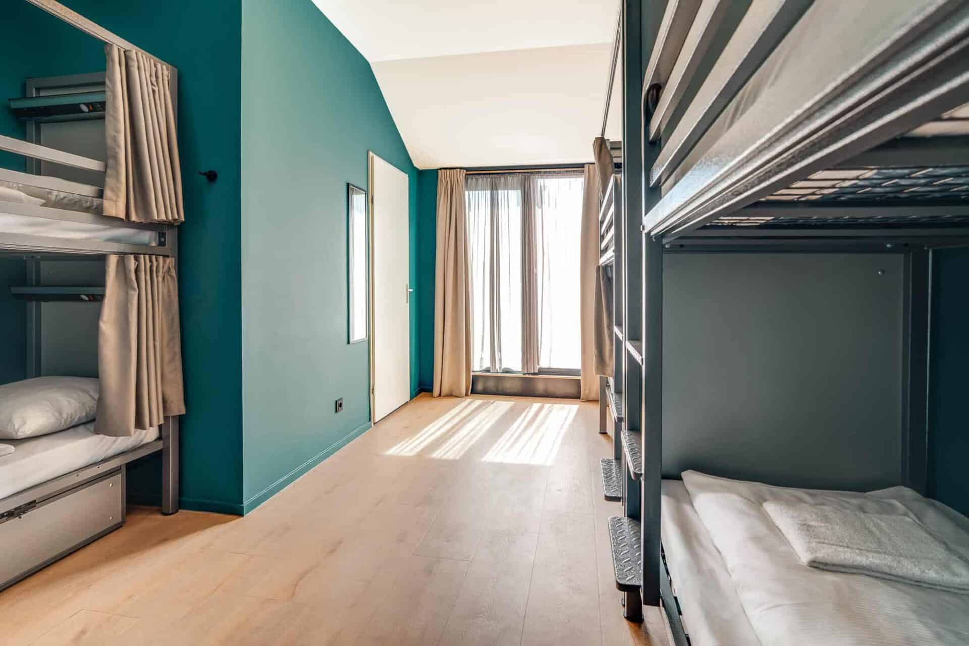 Modern hostel dorm room with bunk beds, large window, and colourful walls in Amsterdam.