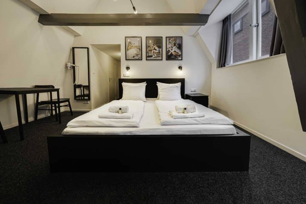 Hostel bedroom with a large double bed, white linens, and contemporary decor in Amsterdam.