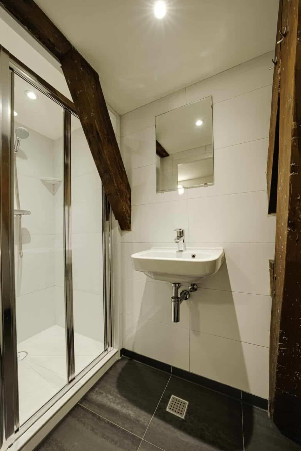 Compact bathroom with shower, sink, and wooden beams at St Christopher’s Amsterdam.