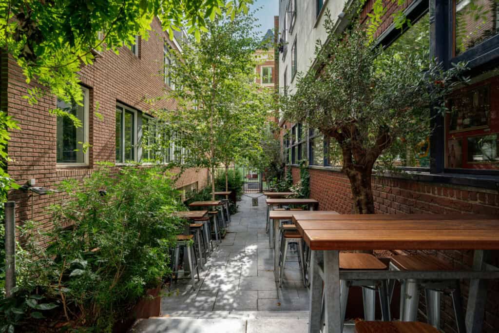 Outdoor seating area at Winston Hostel in Amsterdam with trees and tables.