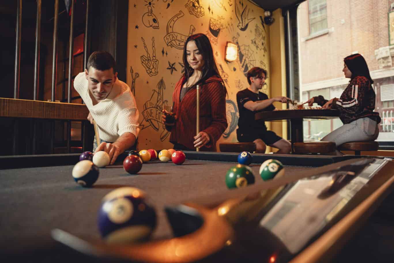 Guests enjoying a game of pool in the lively hostel lounge with modern decor.