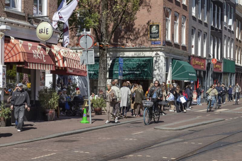 People walk and cycle on the lively Ferdinand Bolstraat in the Amsterdam neighborhood of De Pijp.