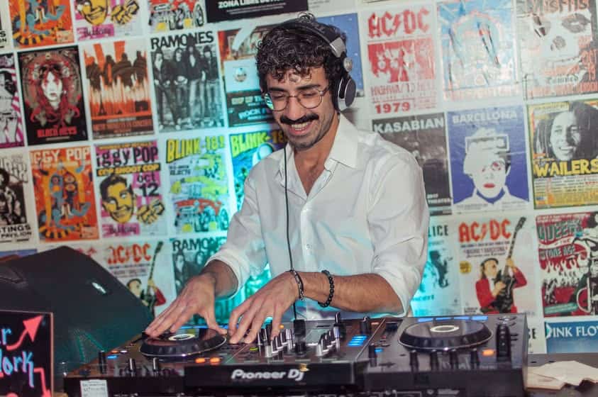 DJ playing music at St Christopher’s Barcelona hostel, with vibrant music posters on the wall behind.