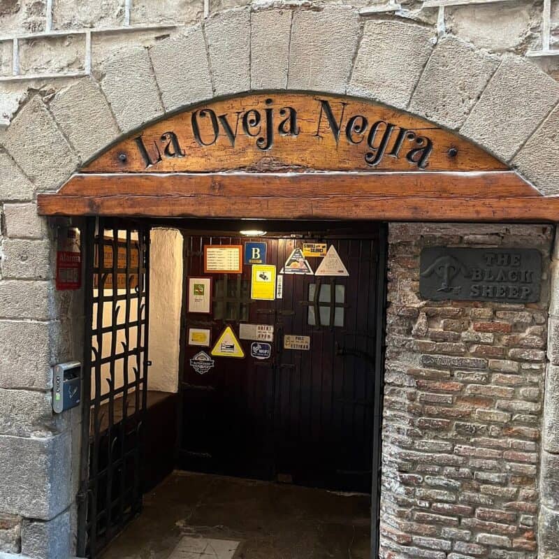 Entrance of La Oveja Negra Hostel in Barcelona, with rustic stone archway and wooden sign.