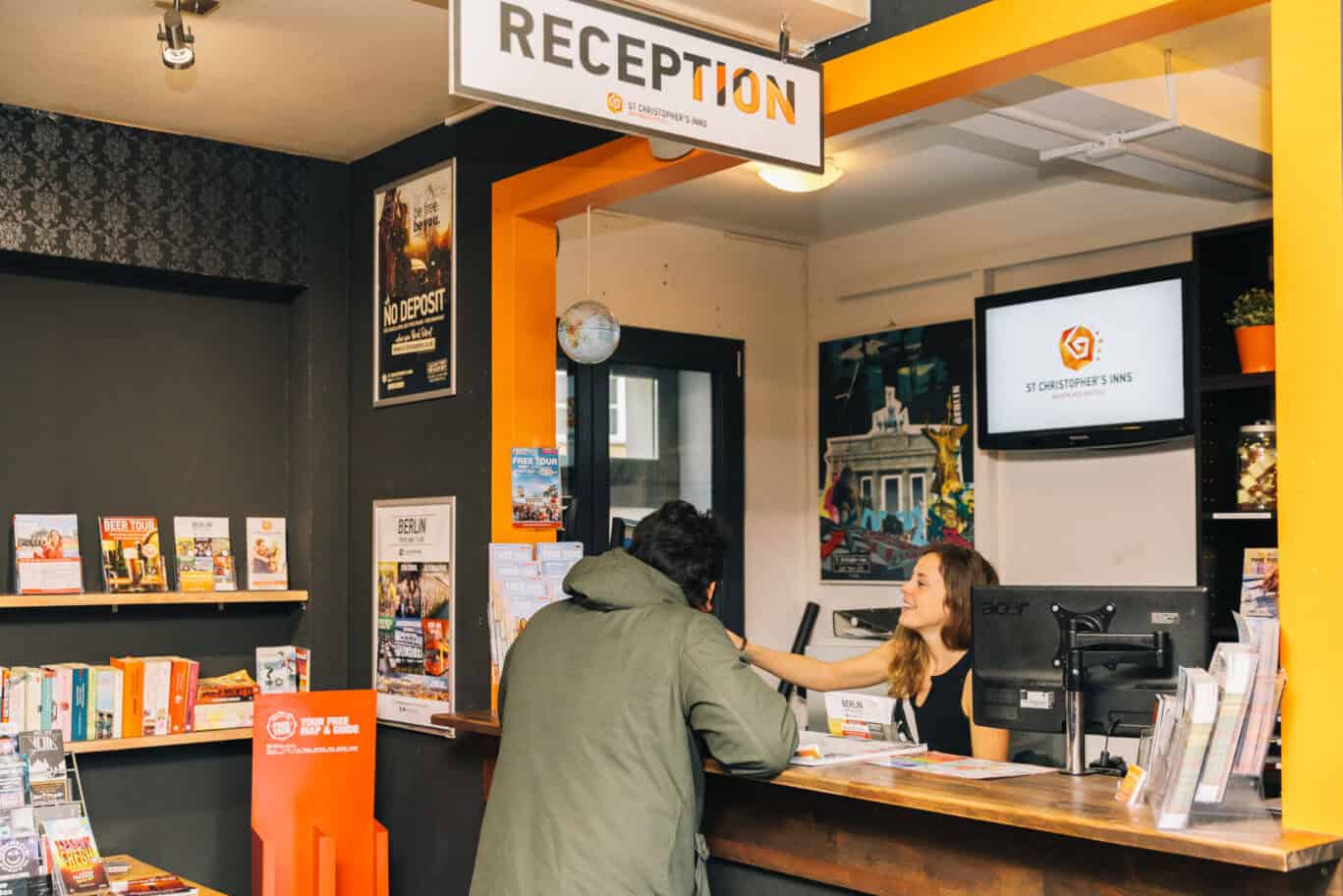 Hostel reception area at Alexanderplatz, Berlin, with staff helping a guest.