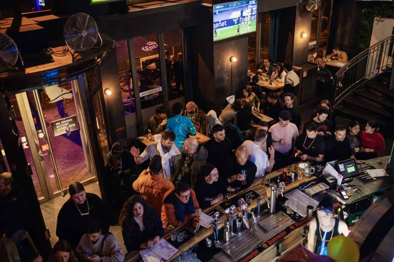 Brightly lit bar with guests enjoying drinks and socialising at Alexanderplatz Hostel, Berlin.