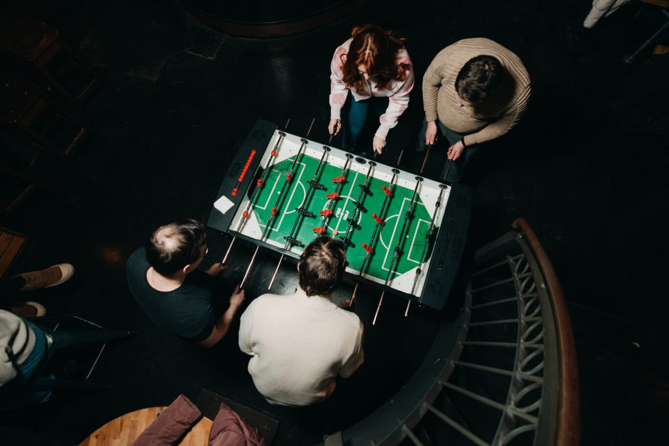 Foosball table with four players engaged in a game at Alexanderplatz hostel, Berlin.