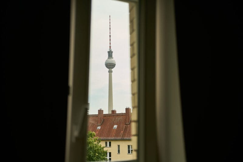 View of Berlin TV Tower through a window with building rooftops in the foreground.