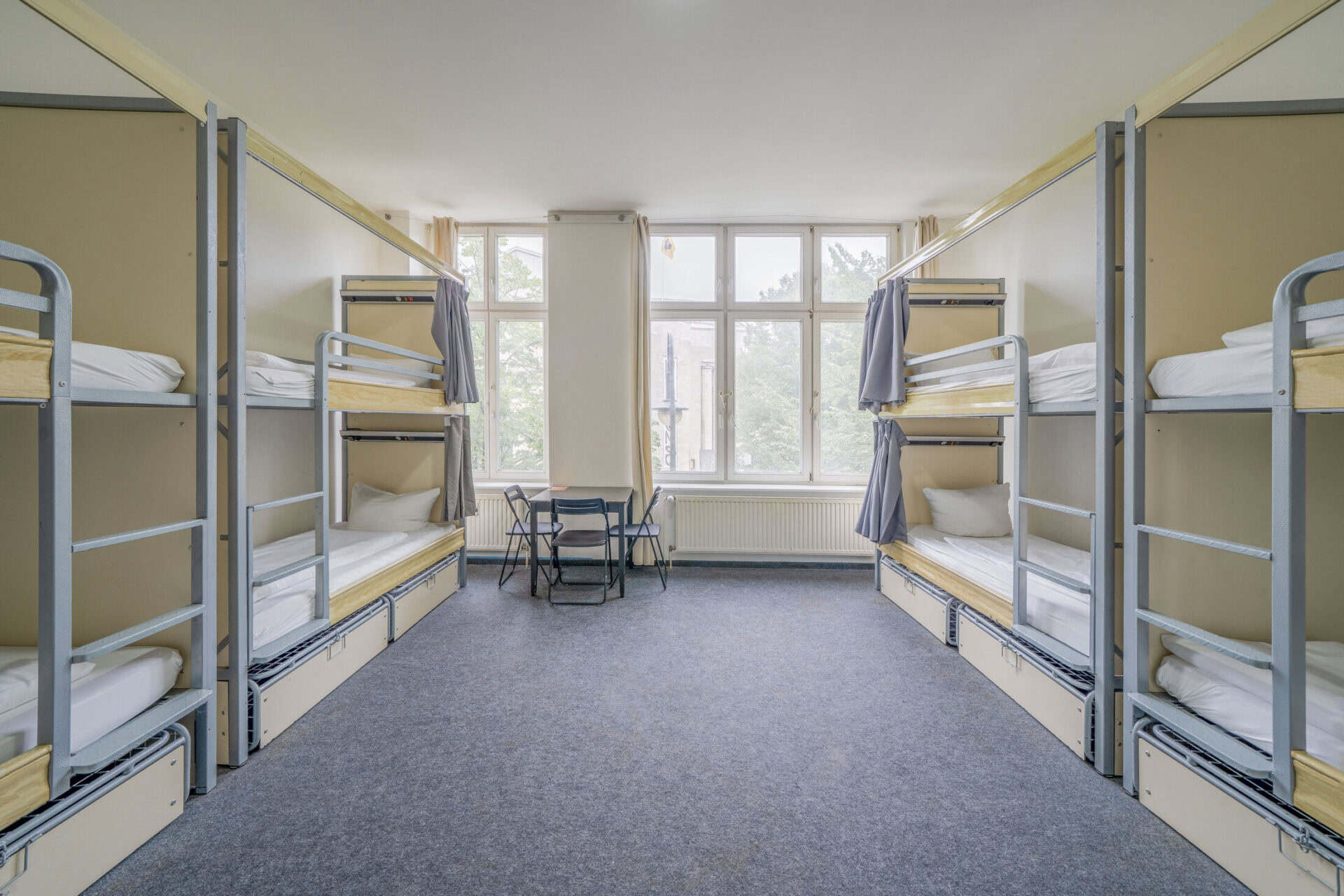 Bunk beds in a bright, spacious hostel dorm room with large windows and natural light.