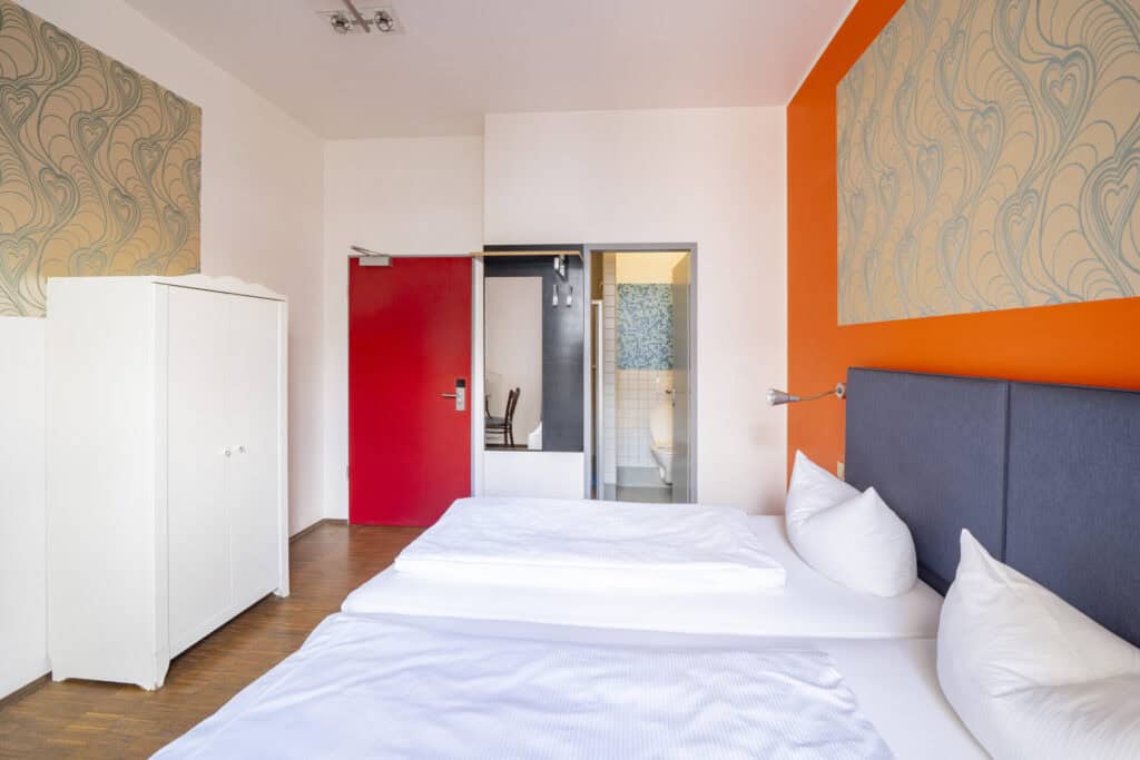 Bright hostel room with two beds, colourful wall accents, and a wardrobe at St Christopher’s Berlin.