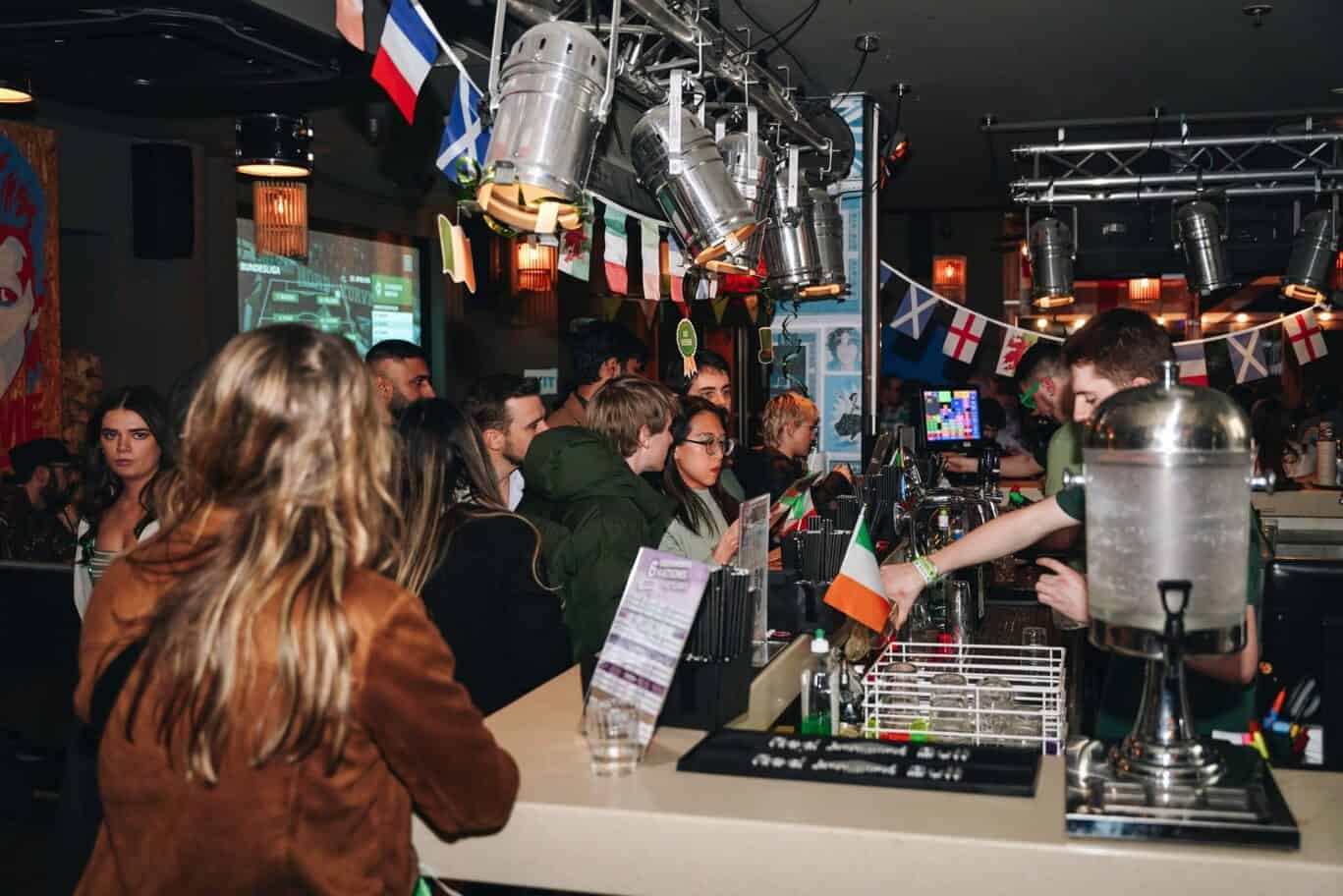 Hostel bar in Berlin with international guests, festive flags, and lively atmosphere at St Christoph.