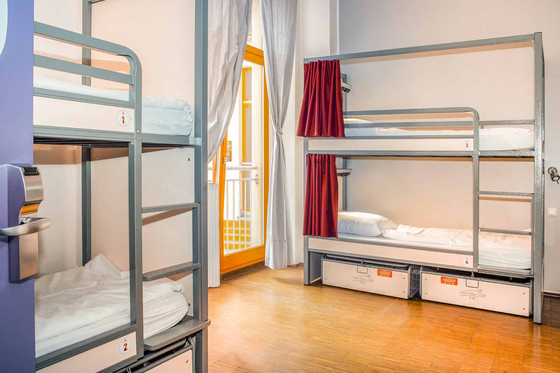 Hostel dorm room with metal bunk beds, bright natural light, and colourful curtains in Berlin Mitte.