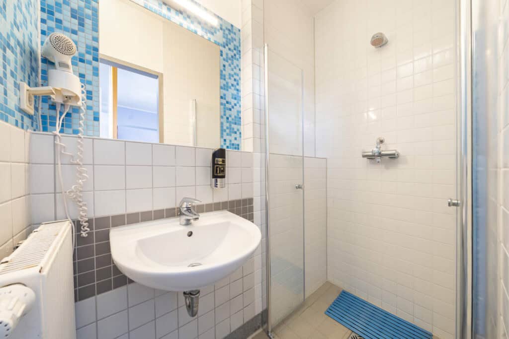 Clean bathroom at St Christopher’s Berlin hostel in Mitte, featuring a sink, mirror, and shower area.