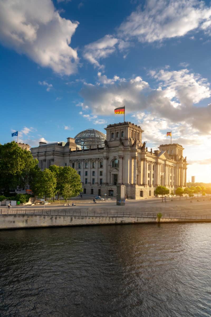 Reichstag building in Berlin with flags, under a partly cloudy sky at sunset.