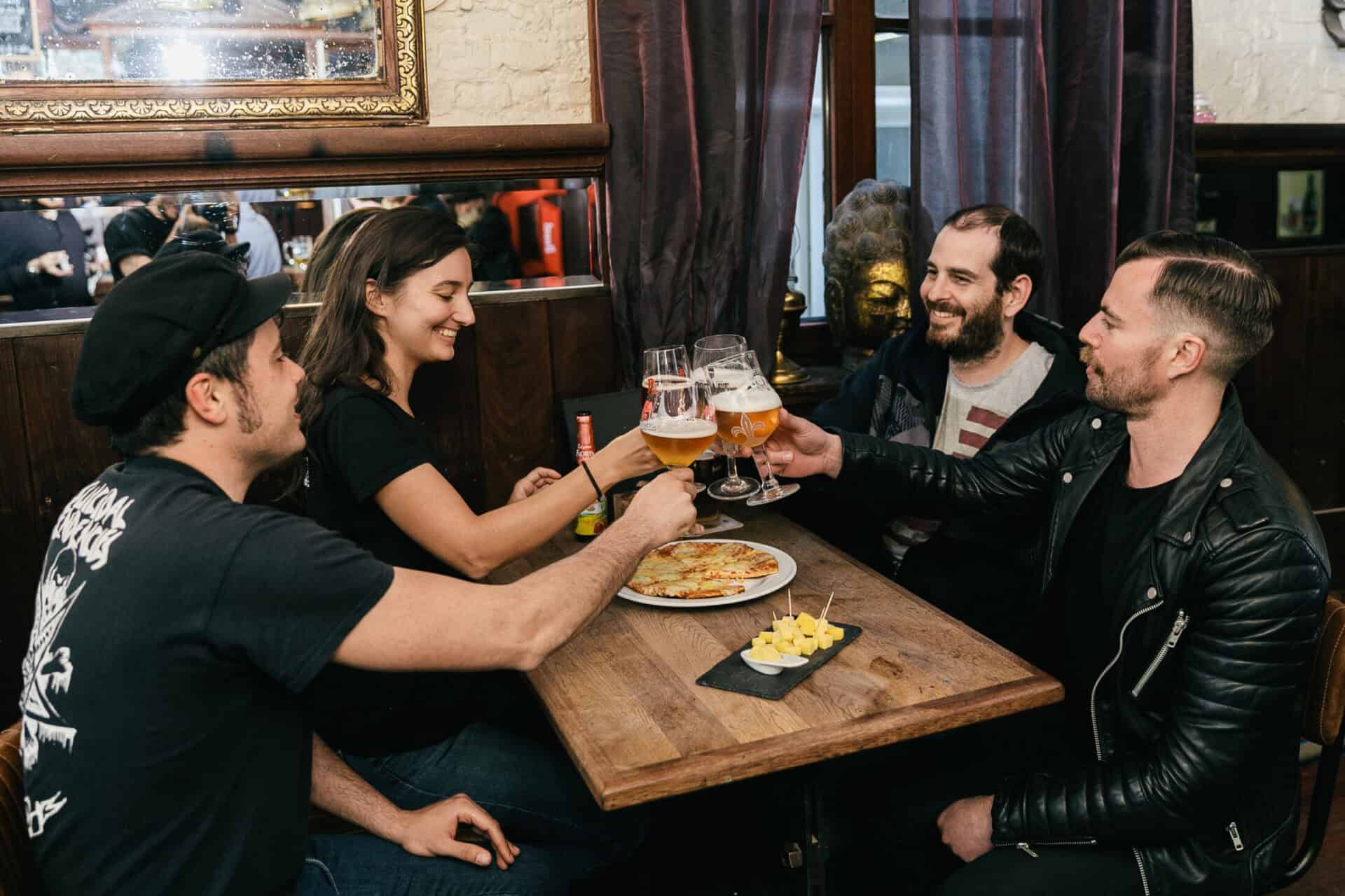 A group of friends clinking glasses of beer and sharing a meal at a cozy pub in Bruges.