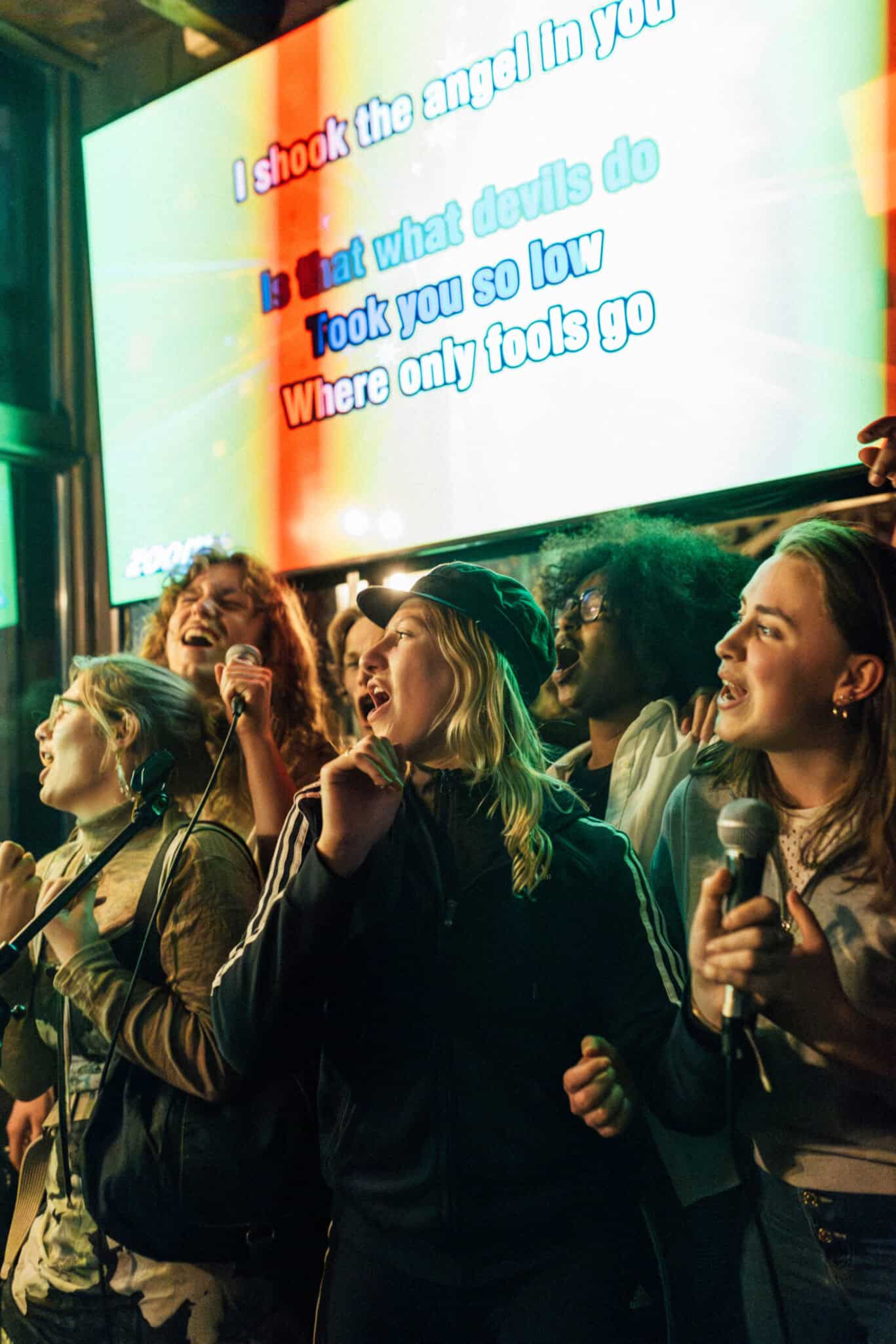 Young people singing karaoke, holding microphones, enjoying a lively night out.