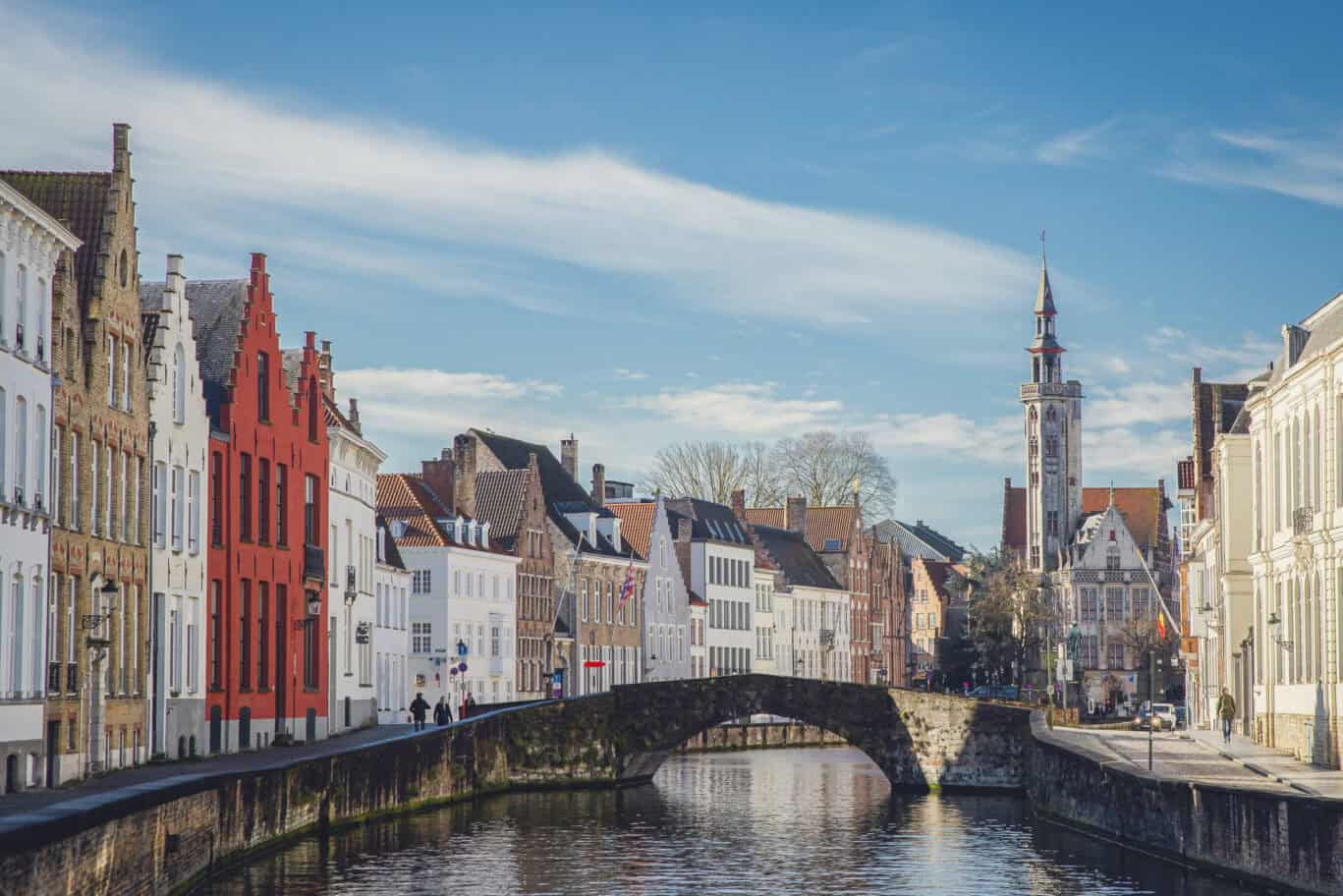 Beautiful view of Bruges canal with colorful historic buildings and a church spire in the background.