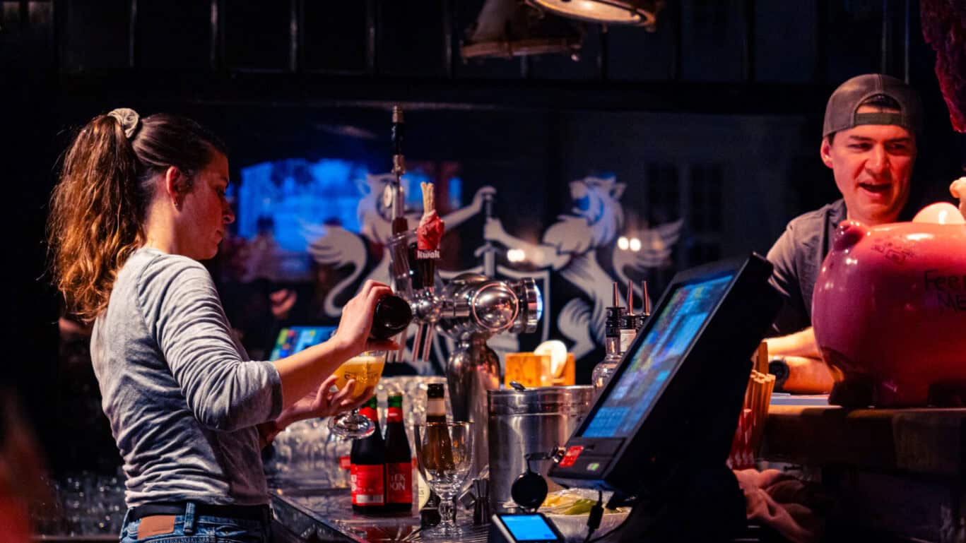 Young woman and man enjoying drinks at the bar in St Christopher’s Bruges hostel.