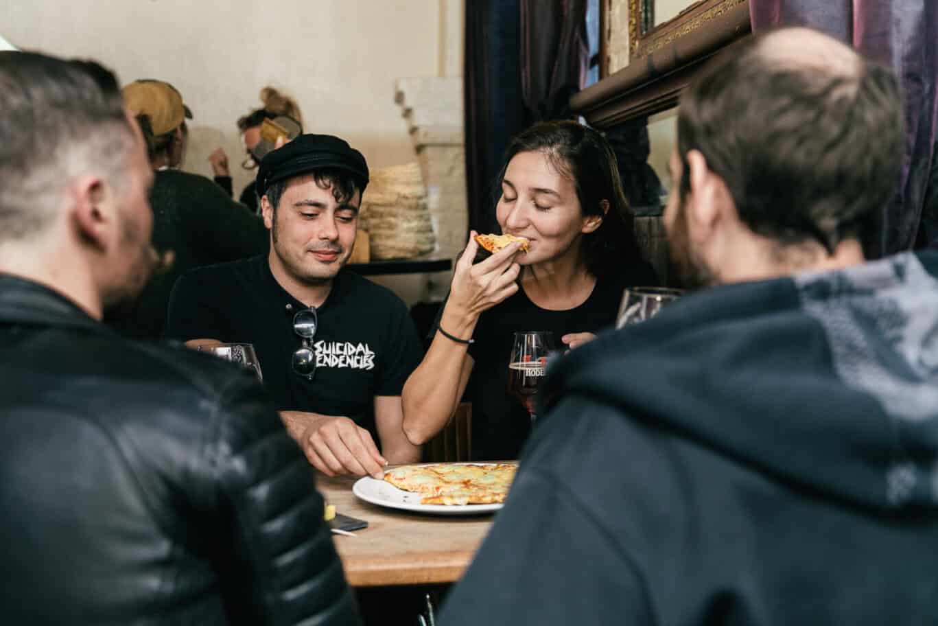 Group of friends sharing a pizza and drinks at a lively social gathering in Bruges.