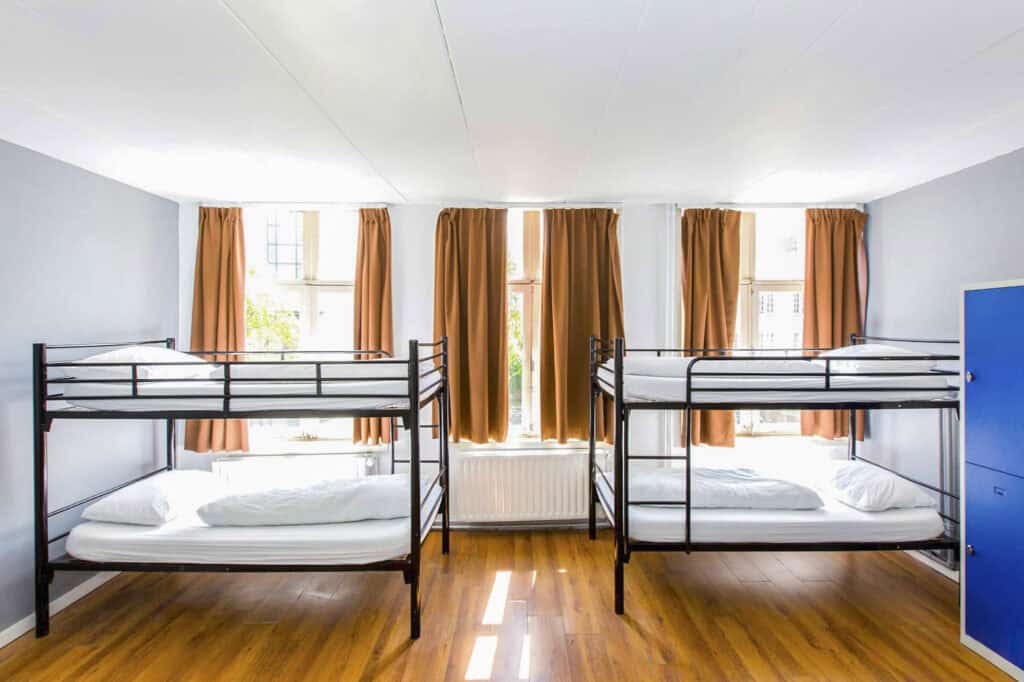 Bright hostel dorm room with bunk beds, large windows, and natural light.