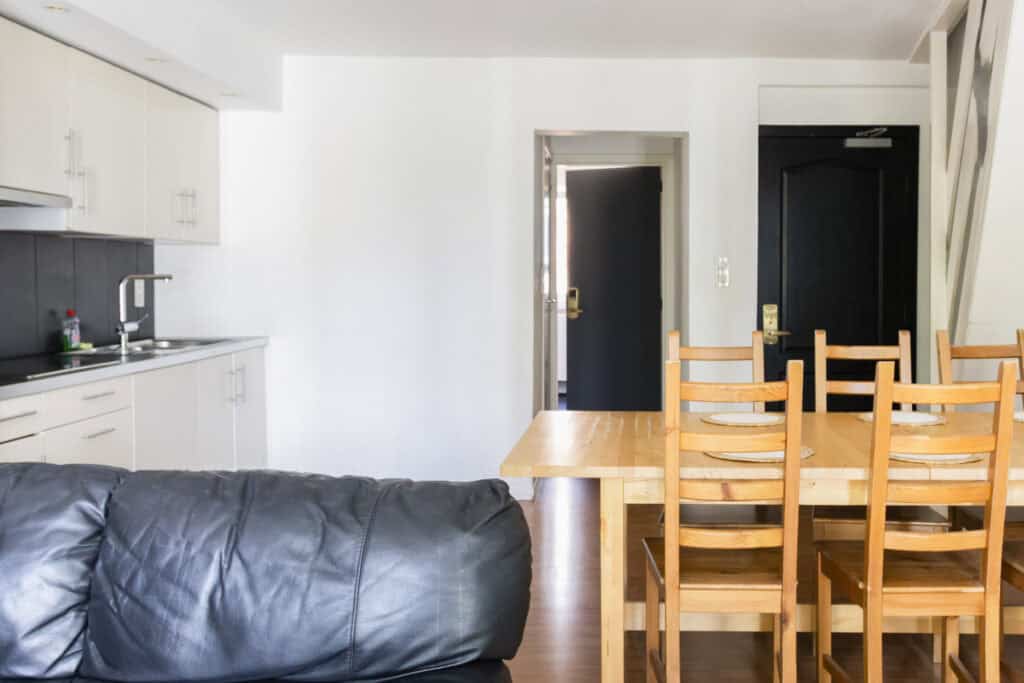 Bright, minimalist kitchen and dining space with wooden furniture in a contemporary hostel setting.