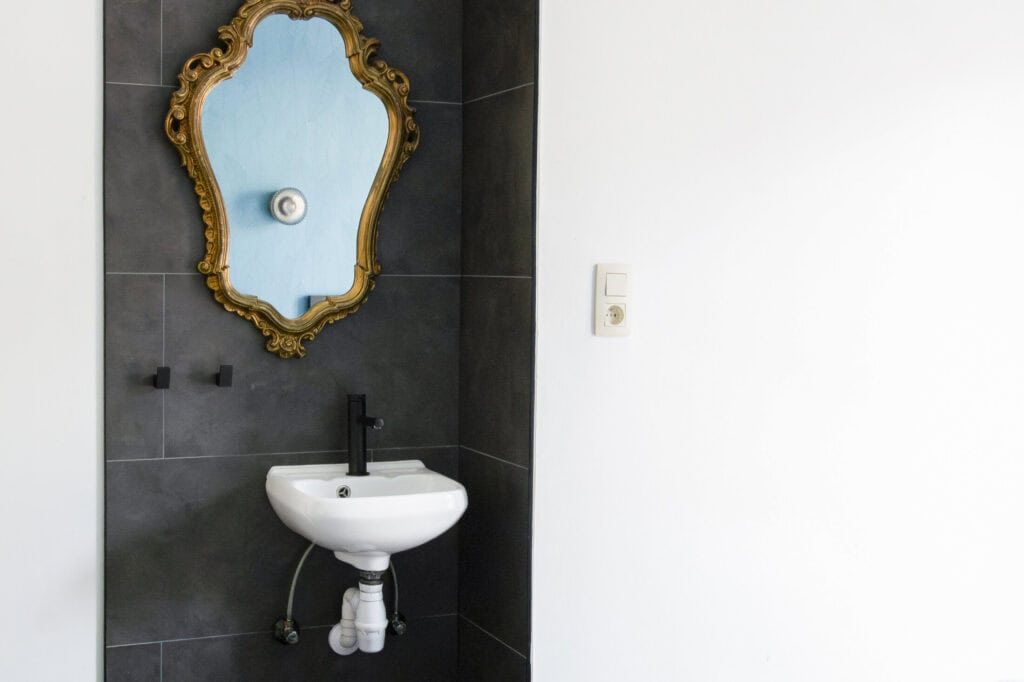 Small bathroom sink with decorative mirror at St Christopher’s Bruges hostel.