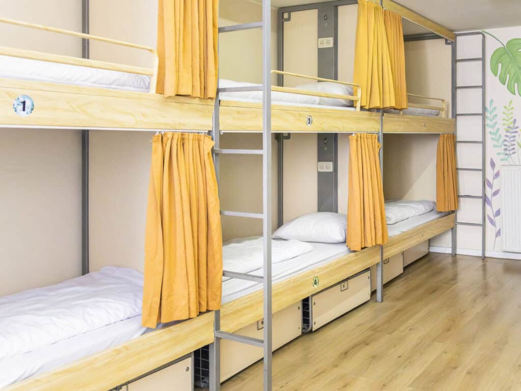 Bright hostel dorm with wooden bunk beds and orange curtains, ideal for budget travellers.
