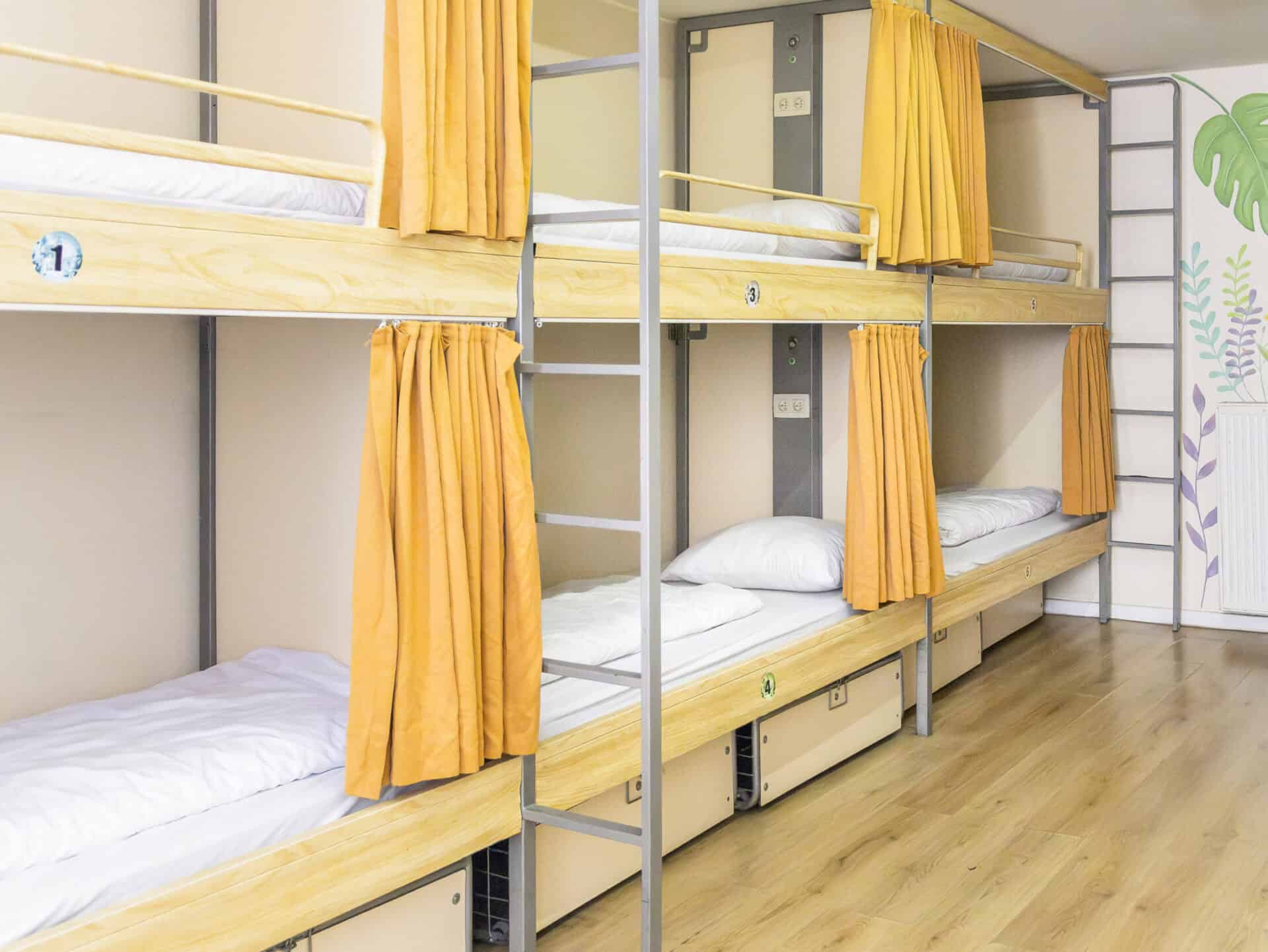 Bright hostel dorm with wooden bunk beds and orange curtains, ideal for budget travellers.