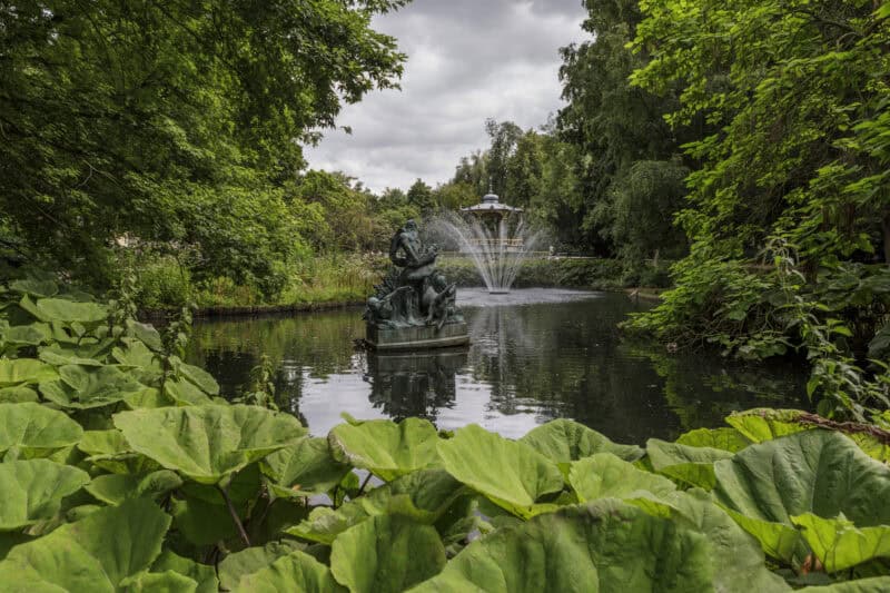 Serene park scene featuring a fountain surrounded by dense trees and vibrant green foliage.