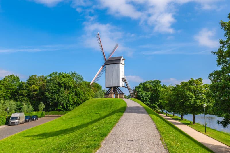 Windmill in Bruges with lush green surroundings and a clear blue sky.