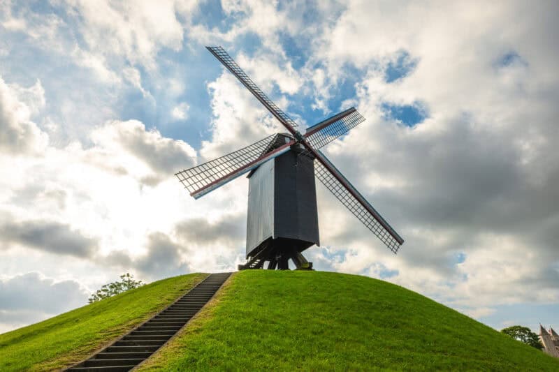 Iconic windmill on a grassy hill in Bruges with a dramatic sky background.