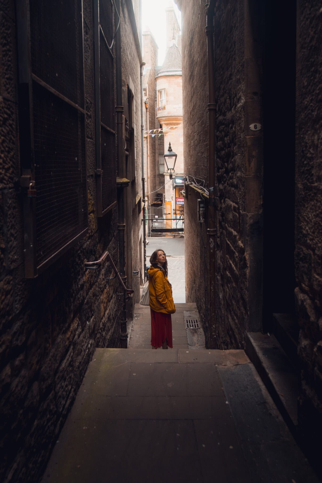 Alleyway in Edinburgh's Old Town with a woman in a yellow jacket standing between historic stone bui.
