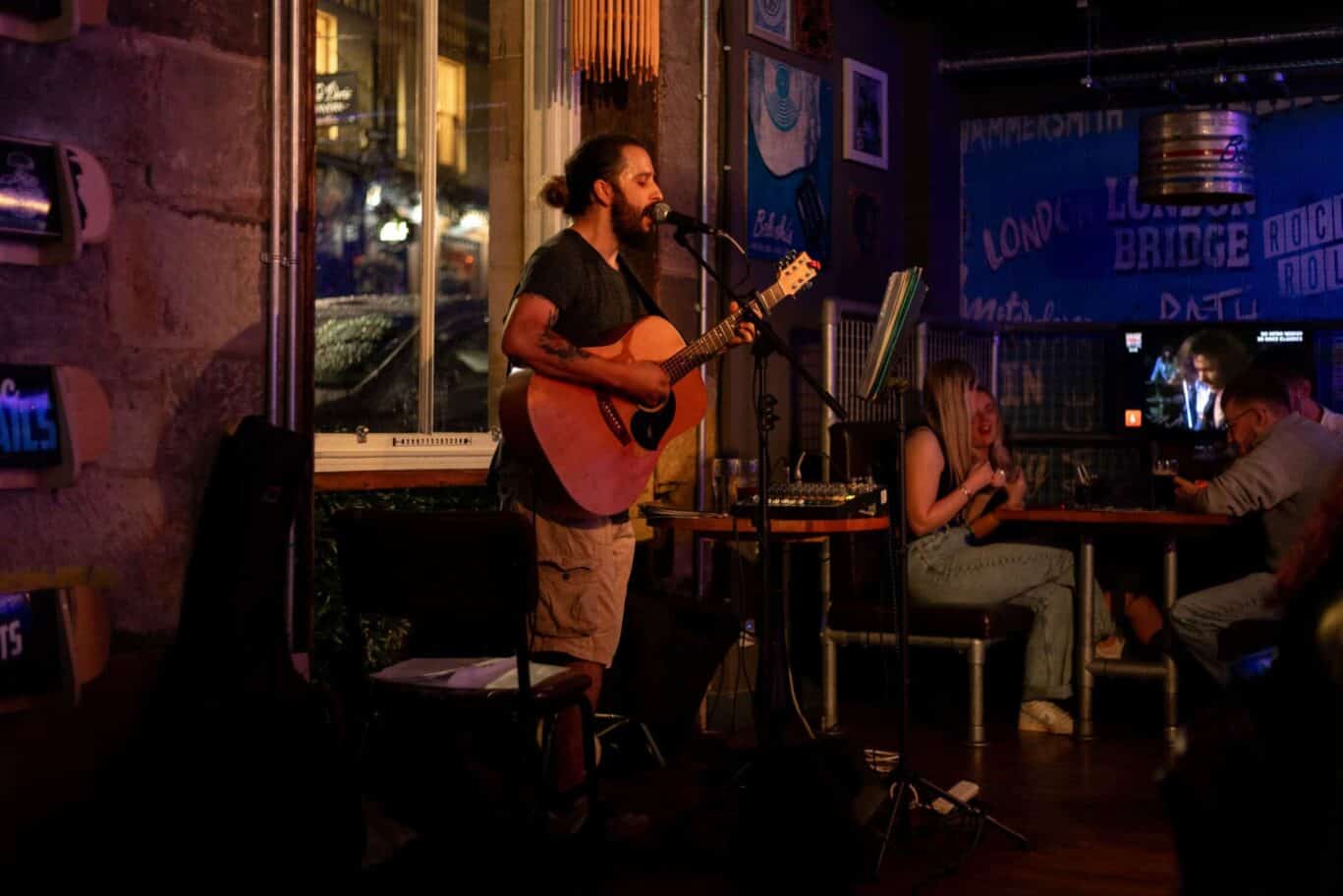 Performing musician with guitar at Edinburgh bar, live entertainment in Old Town.