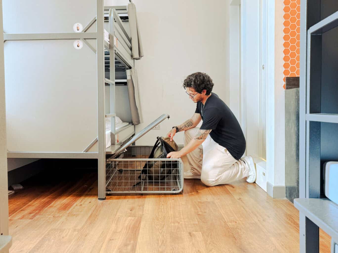 Person placing a pet in a cage under a bunk bed in a hostel room.