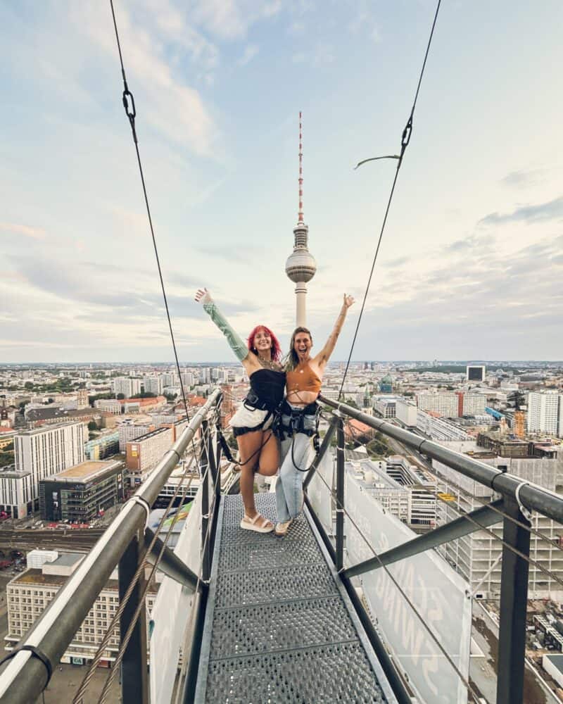 Two women celebrating on the Berlin Skywalk observation deck with city skyline and TV tower in the b.