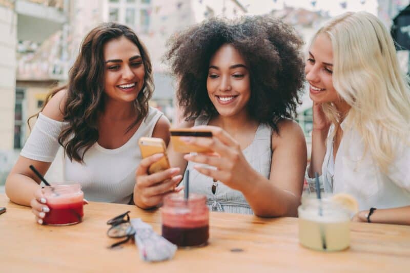 Vibrant group of diverse friends smiling and taking selfies at an outdoor café in Edinburgh.