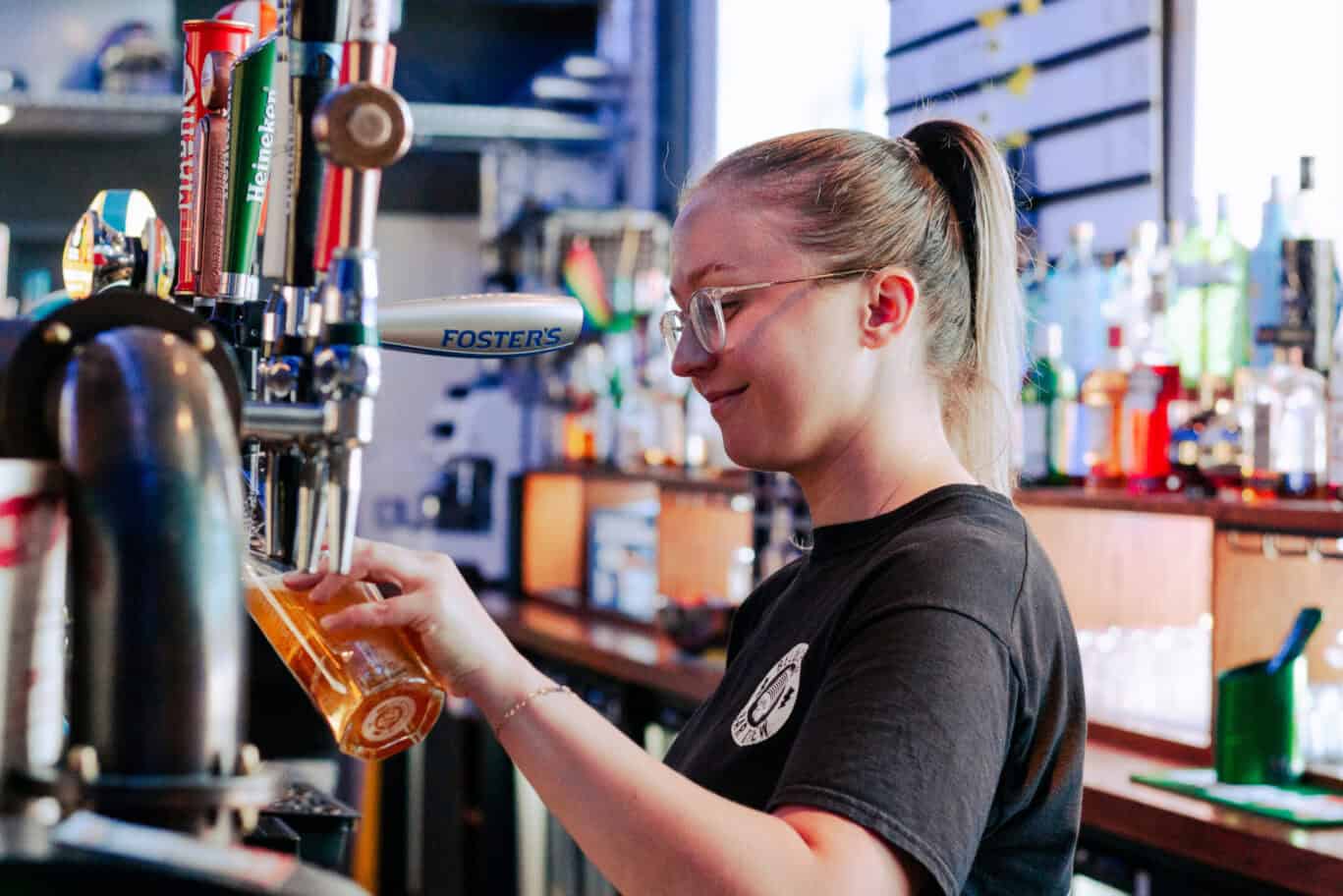 A young female bartender serving beer at the bar in St Christopher’s Edinburgh hostel.
