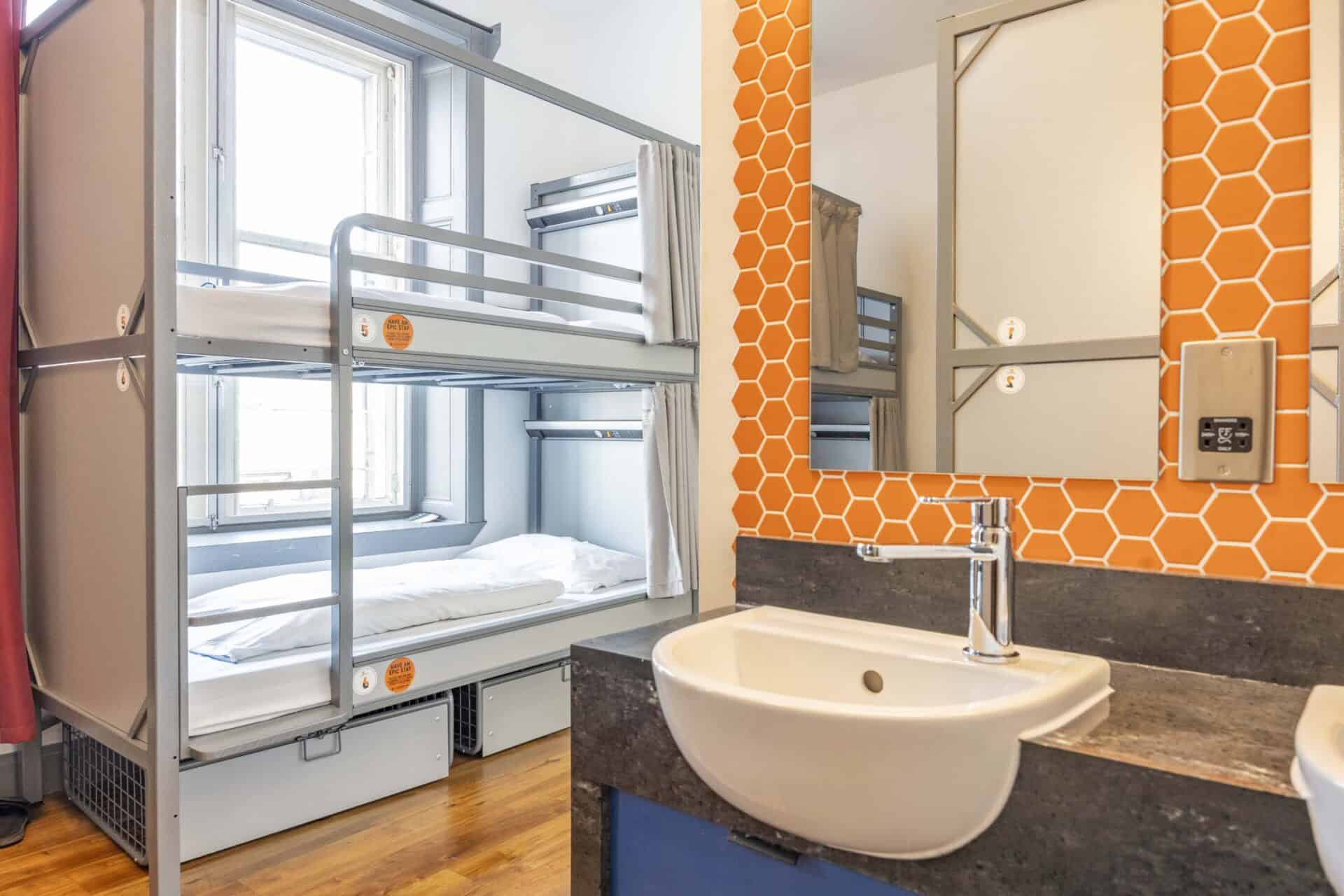 Bright hostel dorm featuring metal bunk beds and large windows for natural light.