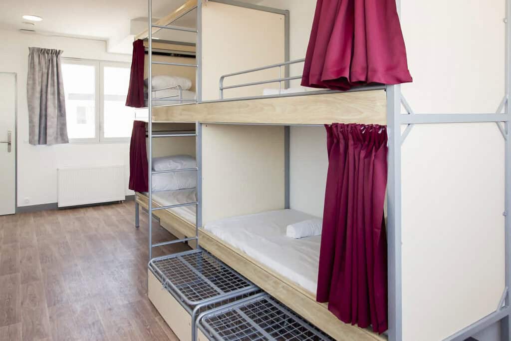 Bunk beds in a hostel dorm room with natural light and red curtains.