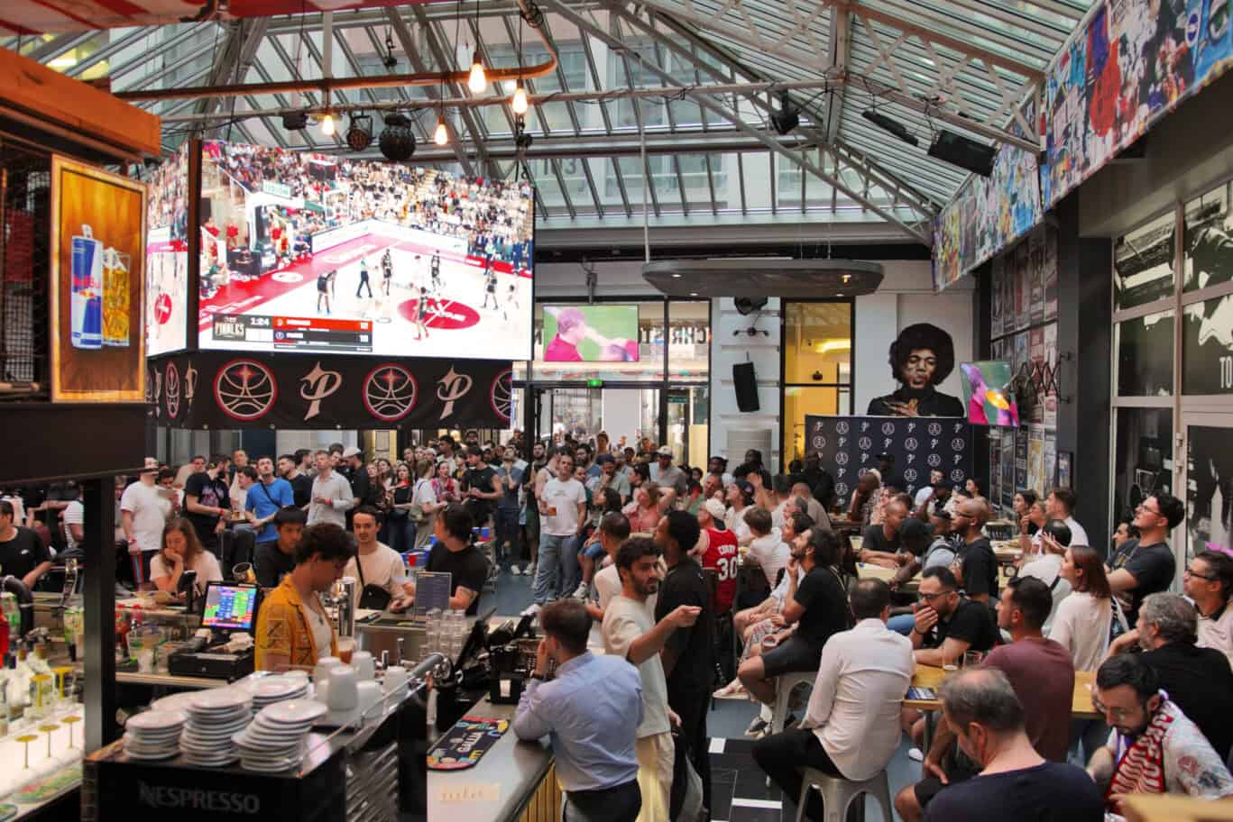 Indoor event at Gare du Nord station with a large crowd and big screen display.